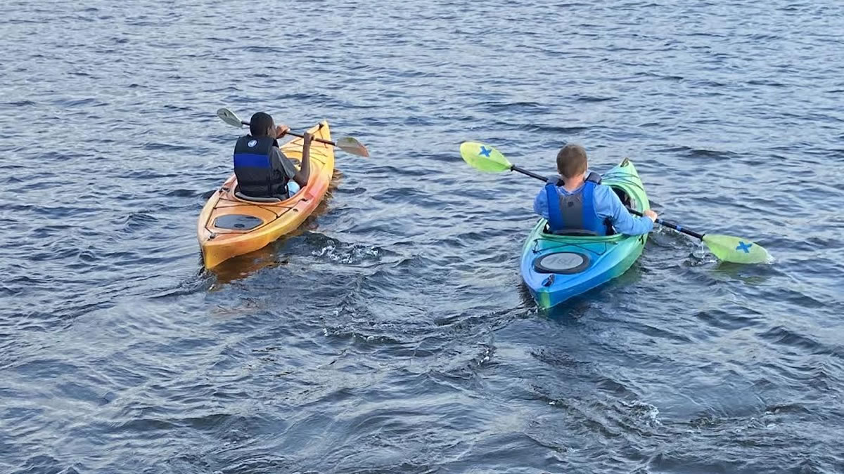 view from the back of two boys in individual kayaks on the water